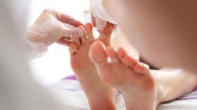 A podiatrist pinching a patient’s toes to test for sensation during an examination.