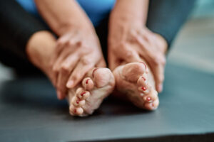 A close-up image of a person holding their bare feet with red-painted toenails, resting on a soft surface.