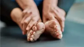 A close-up image of a person holding their bare feet with red-painted toenails, resting on a soft surface.