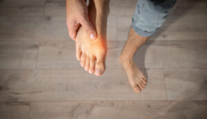 A Caucasian man holding up his right foot and massaging it due to top of foot pain